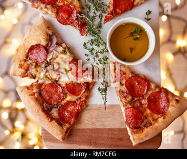 Weihnachten und Neujahr Atmosphäre. Heiße italienische Pizza mit Schmelzen mit Tomate, Salami und Käse auf einem weißen Marmor Schneidebrett. Hintergrund mit Beleuchtung Stockfoto