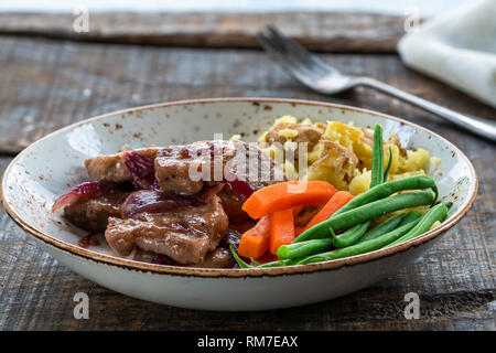 Schweinefleisch in Cranberry Glasur mit roten Zwiebeln, zerdrückte Kartoffeln und gekochtes Gemüse Stockfoto