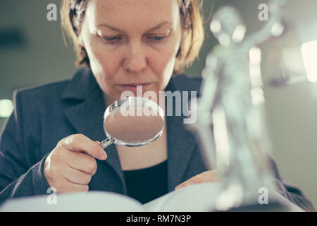 Rechtsanwalt Frau mit Lupe für Gesetz Buch in Ihrem Büro Schreibtisch, selektiven Fokus Stockfoto