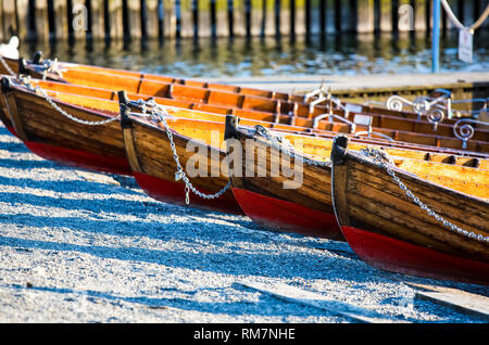 Boote aus Holz mit Ketten stehen auf dem Strand in einer Reihe. Stockfoto