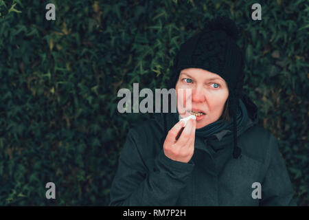 Frau Anwendung Lip Balm auf der Straße an einem kalten Wintertag gegen den gemeinsamen Efeu an der Wand Stockfoto