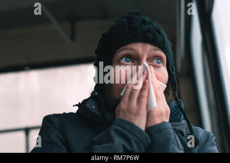 Frau bläst ihre Nase in Papiertaschentuch auf dem Bus an einem kalten Wintertag zu Beginn der Grippesaison Stockfoto