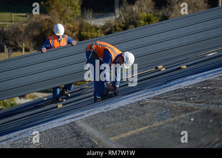 Ein Baumeister Schrauben unten Dach Eisen für das Dach auf eine großes Geschäftshaus in der Nähe von Greymouth, Neuseeland Stockfoto