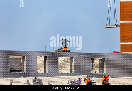 Blick auf die Baustelle mit den Arbeitern über Ziegel und Zement. Blauer Himmel und unvollendete Gebäude Hintergrund. Stockfoto