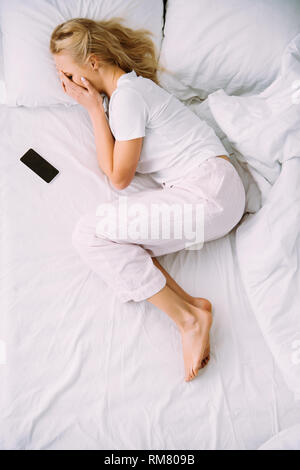 Blick von oben auf die Frau, die Gesicht und schrie, während in der Nähe von Smartphone liegen mit leerer Bildschirm im Bett zu Hause. Stockfoto