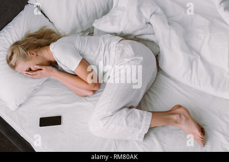 Frau für Gesicht und schrie, während in der Nähe von Smartphone liegen mit leerer Bildschirm im Bett zu Hause. Stockfoto