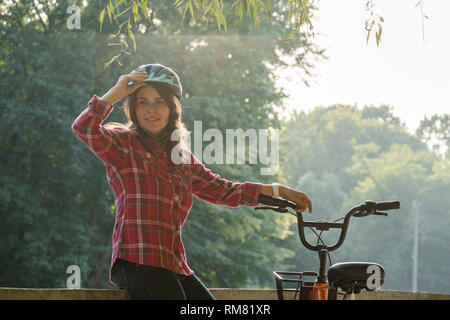 Fach ökologisches Verkehrsmittel Fahrrad. Schöne junge kasazy Frau trägt einen blauen Helm und lange Haare stellt neben eine orange-Farbe Stockfoto