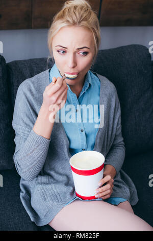 Traurige Frau Eis essen während siitng auf der Couch zu Hause alleine Stockfoto