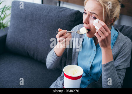 Frau Eis essen und Weinen während siitng auf der Couch zu Hause alleine Stockfoto
