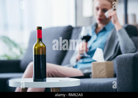 Selektiver Fokus der Weinflasche mit Frau mit einem Glas Wein und wischte sich zu Hause auf Hintergrund Stockfoto