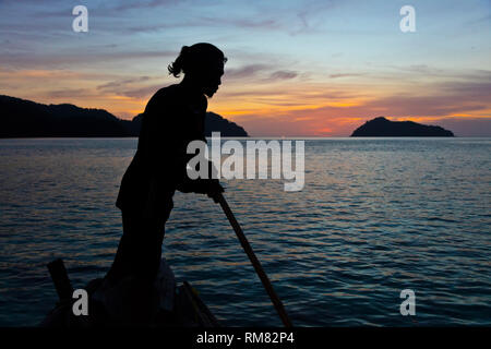 Die MOKEN MANN streers sein Boot an Sonnenuntergänge auf Ko Surin thailändischen Insel in Mu Ko Surin Nationalpark - THAILAND Stockfoto