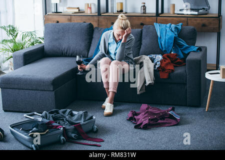 Deprimiert sitzende Frau mit einem Glas Rotwein und Weinen beim Packen im Wohnzimmer nach oben brechen mit Freund Stockfoto