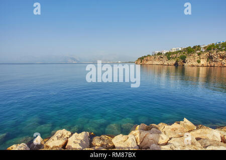 Panorama der Küste Antalyas aus dem hohen Klippe mit Mermerli Strand, Pier, der alte Hafen, moderne Hotels und das Taurusgebirge im Hintergrund, in der Türkei. Stockfoto