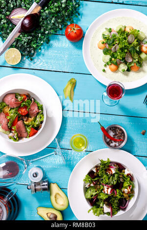 Salate. Schale mit frischen Salaten, Krabben, Fleisch, Tomaten, Olivenöl auf einem Holztisch. Für Text platzieren. Die Aussicht von oben. Traditionelle griechische Gerichte. Stockfoto