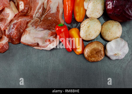 Rohes Fleisch saftige Steaks zum Rösten bereit, verschiedenen Gewürzen, Pfeffer und Kräuter. Platz für Text auf einem schwarzen Brett Hintergrund. Stockfoto