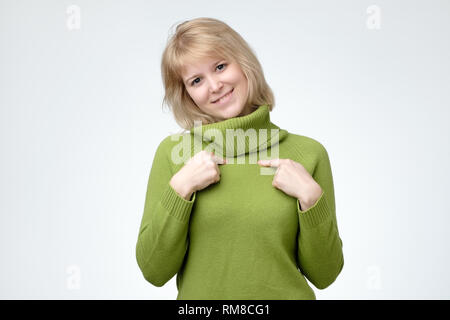 Aufgeregt, staunen Dame im grünen Pullover lächelnd auf sich selbst durch Zeigefinger Stockfoto