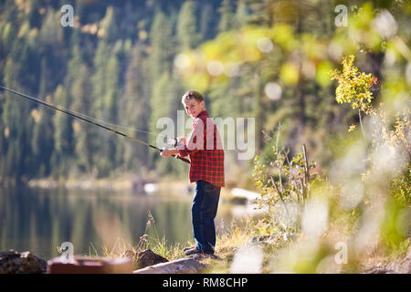 Lächelnde junge Holding eine Angelrute, während die Fischerei am Rande eines Flusses. Stockfoto