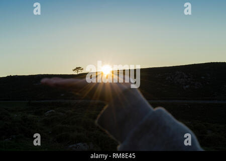 Optische Illusion einer Hand, die Sonne bei Sonnenuntergang in den Bergen