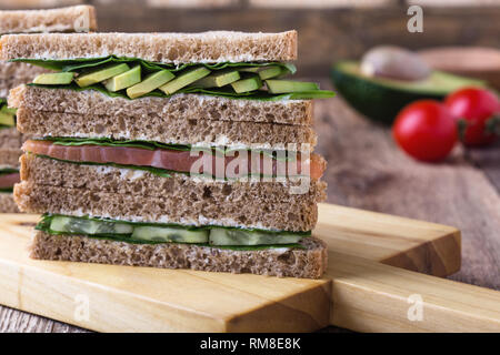 Gesunde vegetarische Sandwiches mit Räucherlachs und grünem Gemüse. Verschiedene Toasts auf Schneidebrett mit rustikalen Holzmöbeln Hintergrund stack, Nahaufnahme, Stockfoto