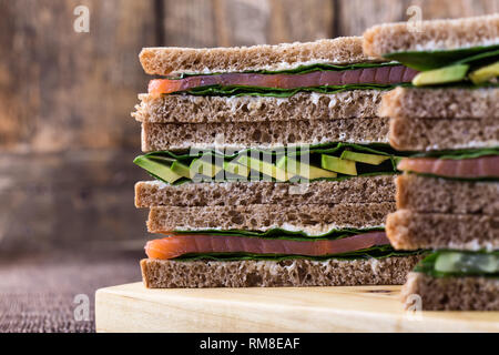 Gesunde vegetarische Sandwiches mit Räucherlachs und grünem Gemüse. Verschiedene Toasts auf Schneidebrett mit rustikalen Holzmöbeln Hintergrund stack, Nahaufnahme, Stockfoto