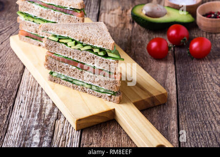 Gesunde vegetarische Sandwiches mit Räucherlachs und grünem Gemüse. Verschiedene Toasts auf Schneidebrett mit rustikalen Holzmöbeln Hintergrund stack, Nahaufnahme, Stockfoto