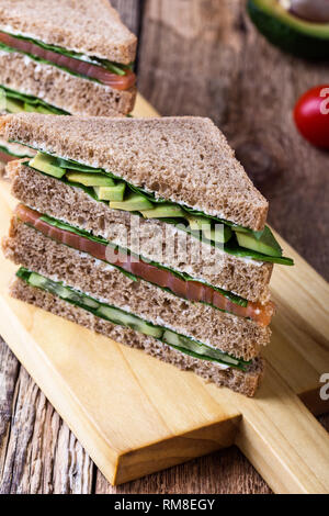 Gesunde vegetarische Sandwiches mit Räucherlachs und grünem Gemüse. Verschiedene Toasts auf Schneidebrett mit rustikalen Holzmöbeln Hintergrund stack, Nahaufnahme, Stockfoto