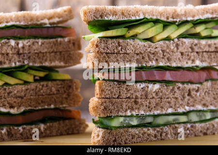 Gesunde vegetarische Sandwiches mit Räucherlachs und grünem Gemüse. Verschiedene Toasts auf Schneidebrett mit rustikalen Holzmöbeln Hintergrund stack, Nahaufnahme, Stockfoto