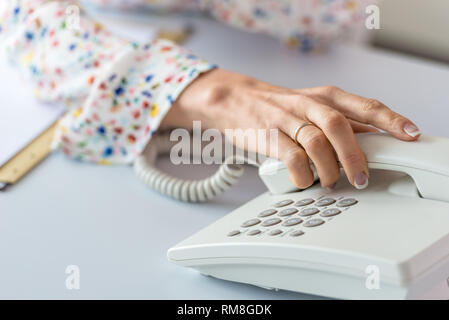 Nahaufnahme des Business Assistant über Sie einen Empfänger von einer weißen Festnetz Telefon. Stockfoto