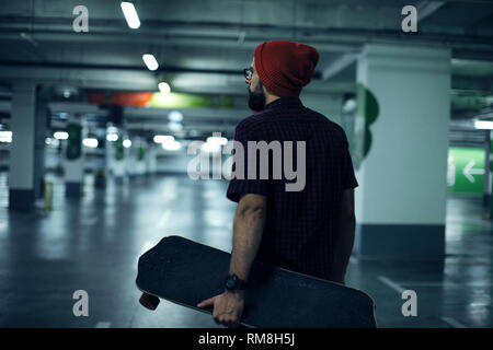 Hipster mit seinem Longboard in der Tiefgarage Stockfoto