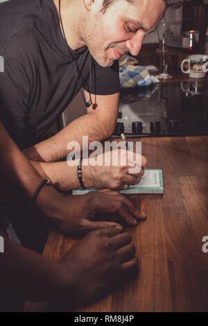 Ein interracial Gay Paare bilden eine Einkaufsliste für Lebensmittel auf einer hölzernen küche top zu Hause. Stockfoto