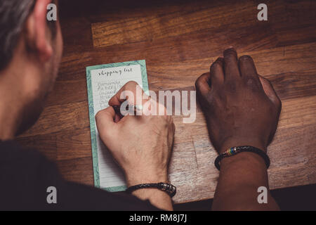 Ein interracial Gay Paare bilden eine Einkaufsliste für Lebensmittel auf einer hölzernen küche top zu Hause. Stockfoto