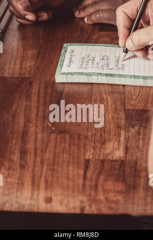 Ein interracial Gay Paare bilden eine Einkaufsliste für Lebensmittel auf einer hölzernen küche top zu Hause. Stockfoto