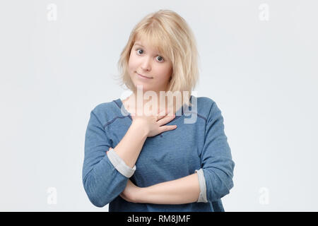 Frau mit blond gefärbten Haaren trägt blaue pulover breit grinsend und halten die Hand auf die Wange Stockfoto