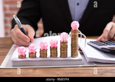 Rosa Sparschwein über Gestapelte Münzen Vor Geschäftsmann Berechnung Rechnung Stockfoto