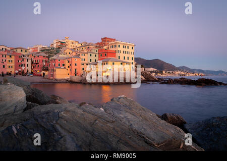 Genua, Italien. Erstaunliches Panorama bei Sonnenuntergang auf dem alten Fischerdorfes Boccadasse mit Blick auf das Meer. Felsen im Vordergrund. Hintergrund mit Li Stockfoto
