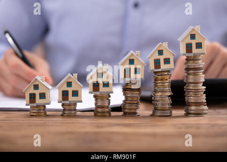 Mittelteil der Geschäftsmann Berechnung Rechnung mit Haus Modelle arrangiert auf Gestapelte Münzen Stockfoto