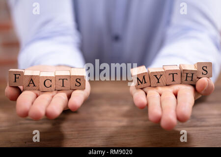 Nahaufnahme der Geschäftsmann Hand Balancing Fakten und Mythen Blöcke über Holz- Schreibtisch Stockfoto