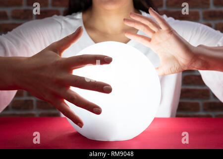 Nahaufnahme der Wahrsager Hand über die glühende Glaskugel Rot Schreibtisch Stockfoto