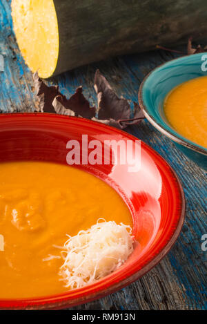 Kürbissuppe mit geriebenem Käse. Kürbis Creme in einer rustikalen Küche auf alten blauen Holztisch, Bild vertikal. Stockfoto