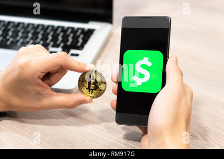 Cash App Logo von Square inc angezeigt auf dem Smartphone durch menschliche Hand neben Bitcoin Münze und Computer Laptop - Slowenien 13.02.2019 Stockfoto