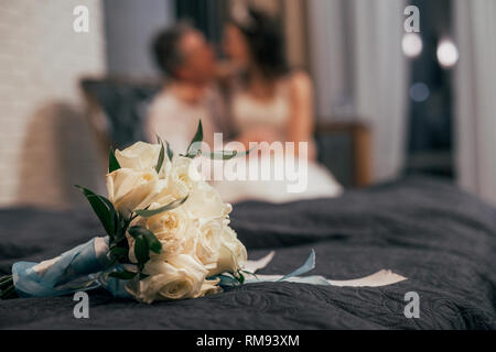 Hochzeit Blumenstrauß aus den weißen Rosen auf das Bett, verschwommenes Paar auf Hintergrund Stockfoto