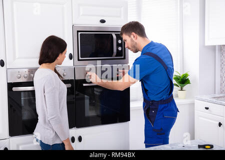 Junge Frau, die in der Nähe von Techniker Reparatur Backofen Stockfoto