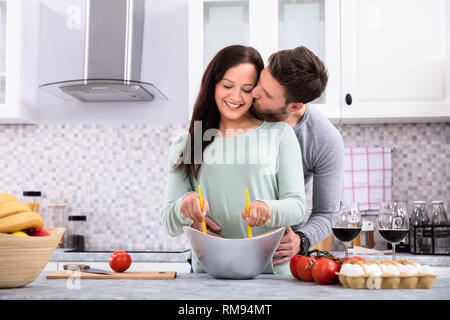 Glücklicher Mann küsste seine Frau, während Sie köstliche frische Lebensmittel in der Küche Stockfoto