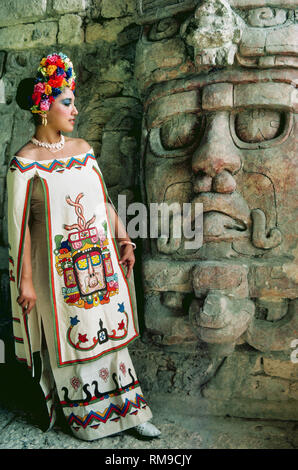 Eine Frau stellt neben einer von fünf gut erhaltene Stuck Masken zu Ehren des Sonnengottes Maya Kin' ich Ahau an Kohunlich, eine archäologische Stätte auf der Halbinsel Yucatán im Bundesstaat Quintana Roo, Mexiko. Das zeitgemäße Design der Maya ihr Kleid porträtiert den 6- bis 8-Fuß-hoch (1,8 bis 2,4 m) Masken, die das zentrale Treppenhaus des 6. Jahrhunderts Pyramide der Tempel der Masken aufgerufen. Stockfoto