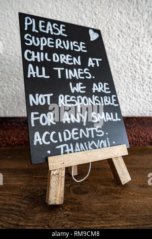 Mini Staffelei mit einer Hand geschrieben "Bitte beaufsichtigen Sie Kinder' Zeichen auf einer Tafel in einer englischen Cafe Stockfoto