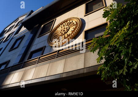 Goldenes Emblem auf dem modernen japanischen Gebäude mit Baum im Vordergrund bei Sonnenuntergang Stockfoto