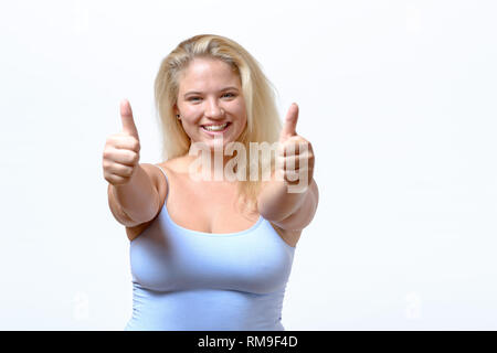 Attraktive vivacious motivierte junge Frau einen Daumen nach oben Geste mit beiden Händen ihre Zustimmung geben oder Signalisierung Erfolg isoliert auf weißem Stockfoto