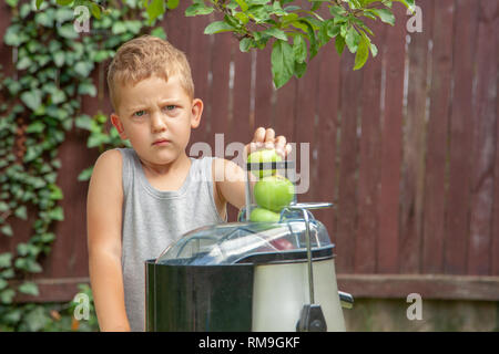 Wütend Kind Junge, Saft aus grünen Äpfel im Entsafter im Freien. Stockfoto