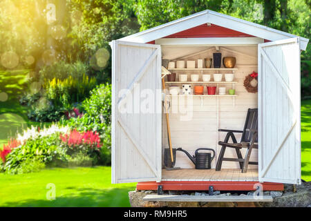 Gartenhaus mit Gartengeräte gefüllt. Schaufeln, Rechen, Töpfe, Wasser Krug in die Hütte. Grünen sonnigen Garten im Hintergrund. Stockfoto