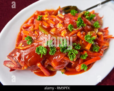 Ein ganzer gebratener red snapper Fisch mit süß-saurer Soße, mit Petersilie dekoriert, bereit, auf einem weißen Teller zu essen, in den Philippinen gesehen Stockfoto